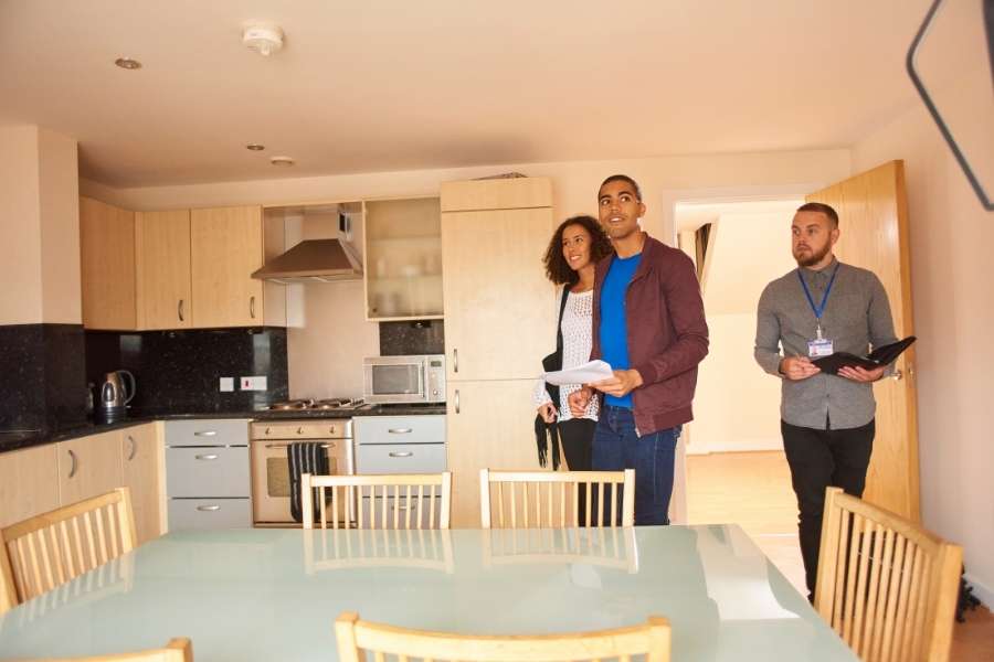 Agent immobilier guidant un couple lors d'une visite immobilière dans une cuisine moderne.