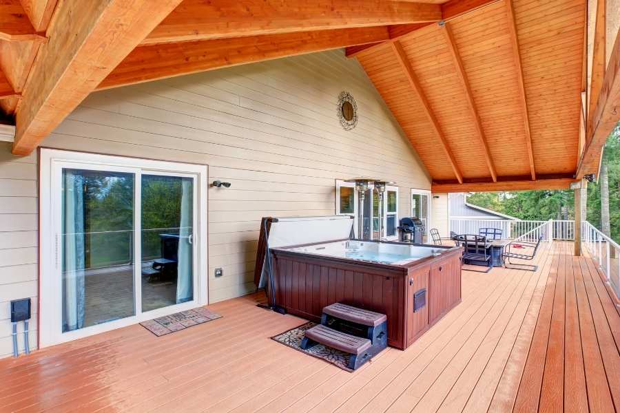 Une grande terrasse en bois avec un jacuzzi et un coin repas pour aménager un coin détente complet.