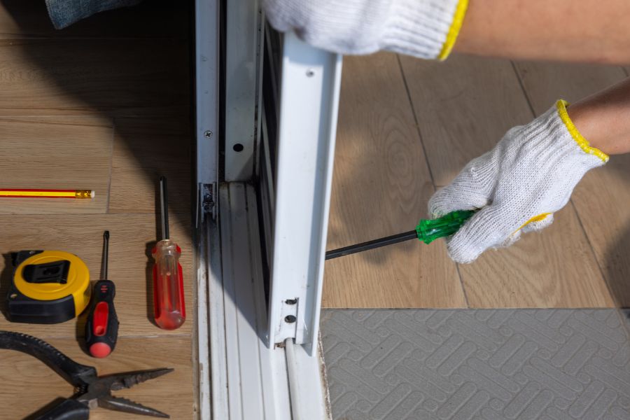 Des outils de bricolage disposés au sol près d'un rail de menuiserie coulissante, représentant la réparation d'une serrure de portail coulissant qui déraille.