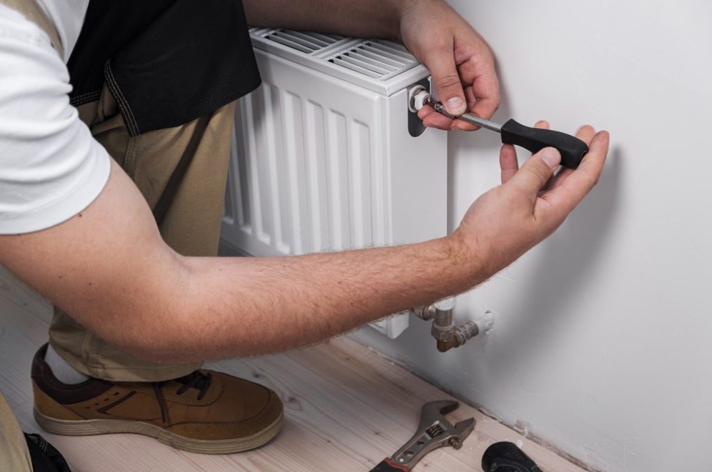 Un technicien utilise un tournevis pour purger ou ajuster un radiateur lors des travaux visant à remplacer ancien chauffage central.